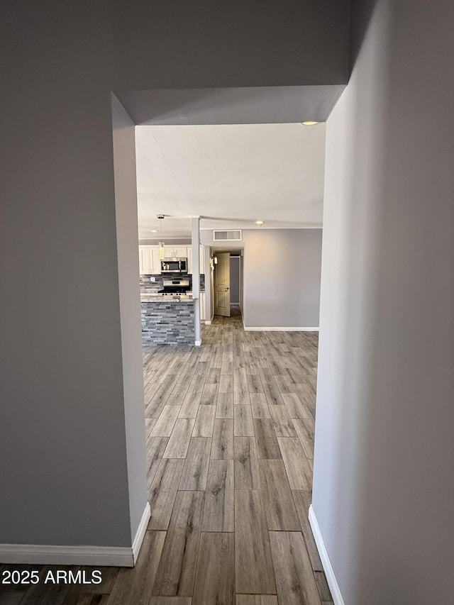 hallway with baseboards, visible vents, and wood finished floors