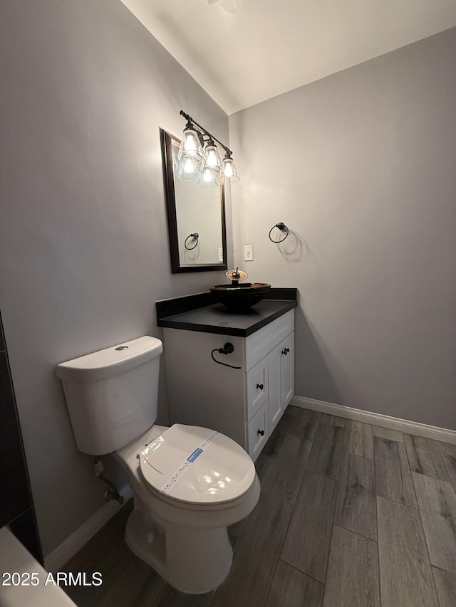 half bath with toilet, baseboards, wood finished floors, and vanity