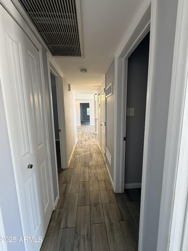 hallway featuring dark wood-type flooring, baseboards, and visible vents