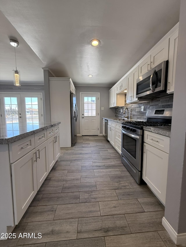 kitchen with stainless steel appliances, white cabinetry, light stone counters, and wood finish floors