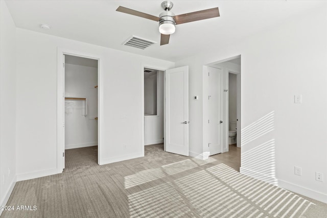 unfurnished bedroom with ceiling fan, ensuite bathroom, a walk in closet, light carpet, and a closet