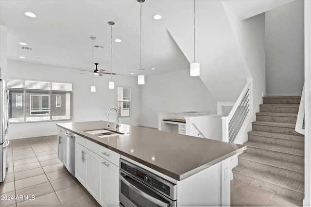 kitchen with ceiling fan, a kitchen island with sink, sink, white cabinetry, and hanging light fixtures