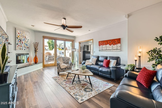 living room featuring hardwood / wood-style flooring, ceiling fan, ornamental molding, and a textured ceiling