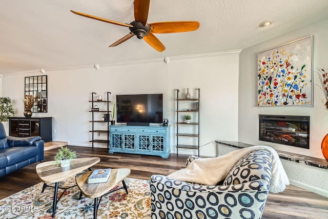 living room featuring ceiling fan, wood-type flooring, ornamental molding, and a textured ceiling