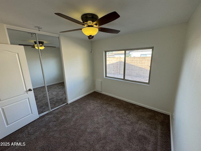 unfurnished bedroom with dark colored carpet, ceiling fan, and a closet