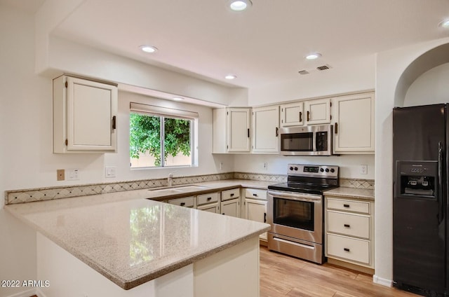 kitchen featuring sink, appliances with stainless steel finishes, light stone counters, light hardwood / wood-style floors, and kitchen peninsula