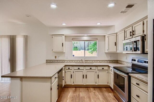 kitchen featuring appliances with stainless steel finishes, sink, kitchen peninsula, and light hardwood / wood-style flooring