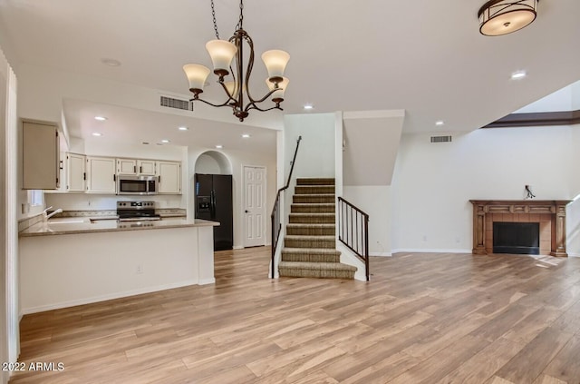 kitchen featuring light wood-type flooring, a chandelier, stainless steel appliances, kitchen peninsula, and pendant lighting