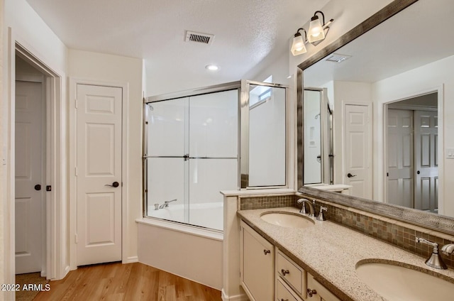 bathroom featuring a textured ceiling, shower / bath combination with glass door, dual bowl vanity, and hardwood / wood-style flooring