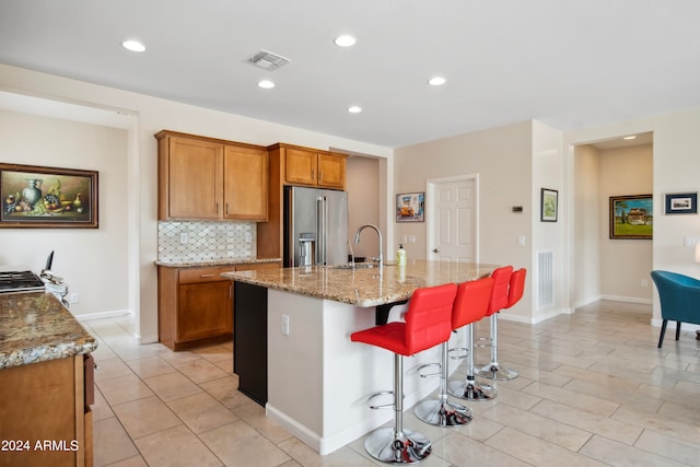 kitchen with a kitchen bar, backsplash, an island with sink, light tile patterned flooring, and high quality fridge