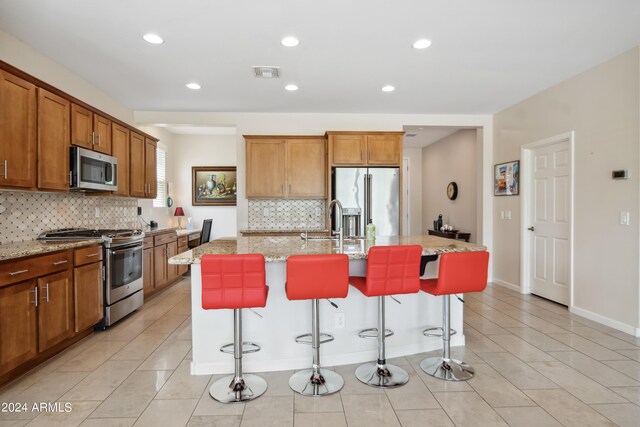 kitchen with a kitchen island with sink, light stone countertops, backsplash, and stainless steel appliances