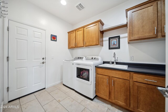 washroom with light tile patterned flooring, sink, washing machine and dryer, and cabinets