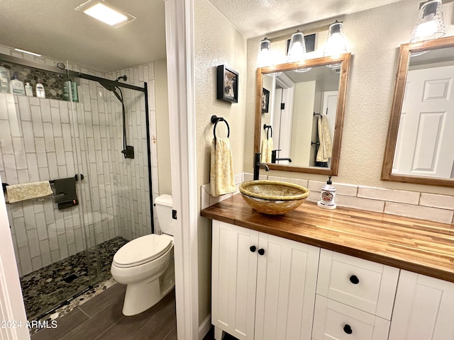 bathroom featuring a textured ceiling, vanity, toilet, and a shower with shower door