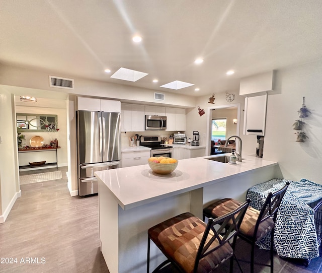 kitchen featuring a skylight, white cabinetry, sink, a kitchen bar, and appliances with stainless steel finishes