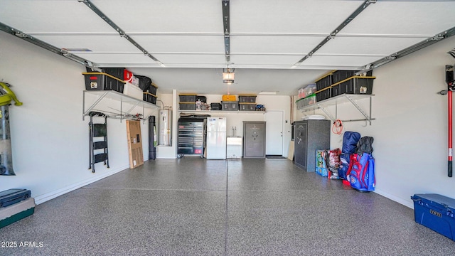 garage featuring water heater, baseboards, a garage door opener, and freestanding refrigerator