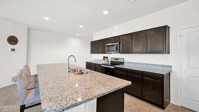 kitchen featuring stainless steel appliances, a sink, a kitchen island with sink, and light stone countertops