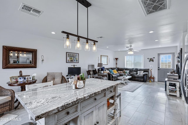 kitchen with hanging light fixtures, ceiling fan, light tile patterned floors, a kitchen island, and light stone counters