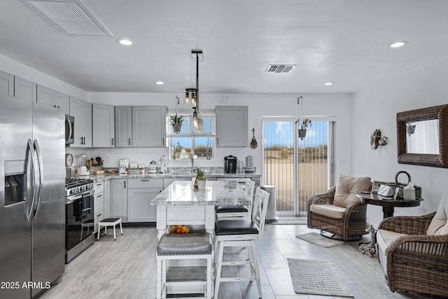 kitchen with a center island, a kitchen breakfast bar, hanging light fixtures, light stone countertops, and appliances with stainless steel finishes