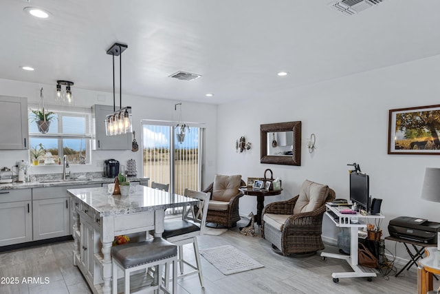 kitchen with a center island, sink, hanging light fixtures, a kitchen bar, and gray cabinets