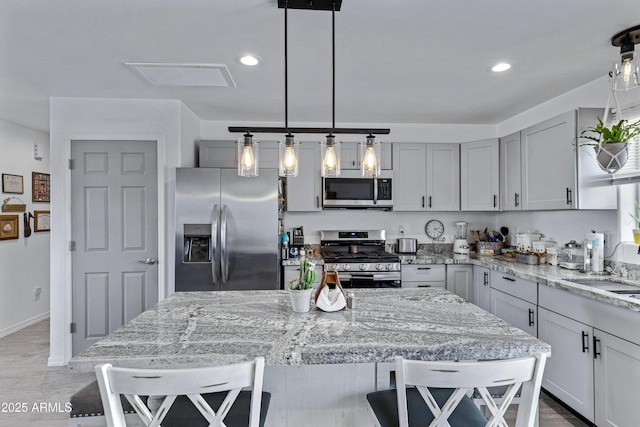 kitchen featuring a breakfast bar, appliances with stainless steel finishes, light stone countertops, and hanging light fixtures