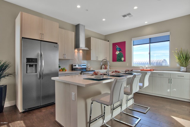 kitchen with stainless steel appliances, dark wood-type flooring, wall chimney exhaust hood, and an island with sink