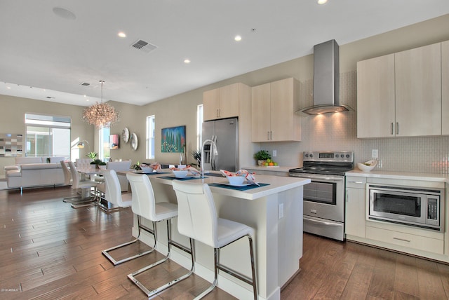 kitchen featuring decorative light fixtures, a breakfast bar, appliances with stainless steel finishes, tasteful backsplash, and wall chimney range hood