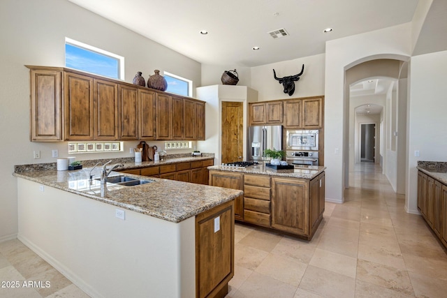 kitchen featuring visible vents, light stone counters, brown cabinets, stainless steel appliances, and a sink