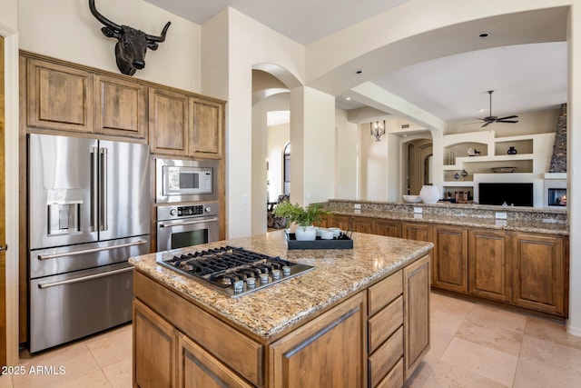 kitchen with light stone countertops, open floor plan, arched walkways, stainless steel appliances, and a ceiling fan