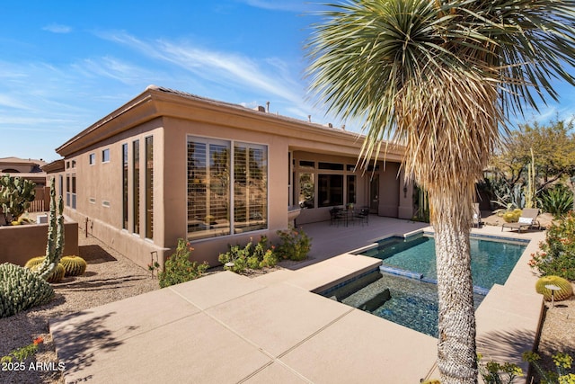 rear view of property featuring an in ground hot tub, stucco siding, an outdoor pool, and a patio