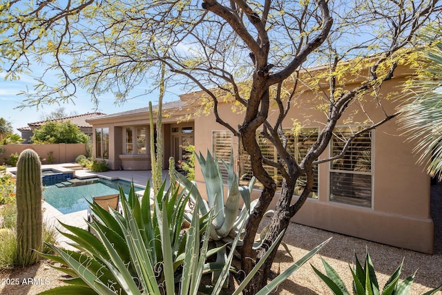 rear view of house featuring stucco siding, fence, a patio, and a fenced in pool