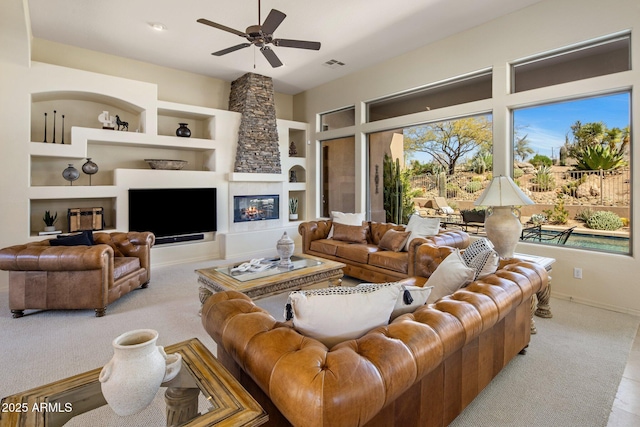 carpeted living area featuring built in shelves, baseboards, visible vents, a fireplace, and ceiling fan