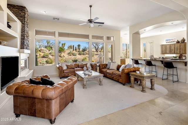 living area featuring arched walkways, visible vents, a large fireplace, and ceiling fan