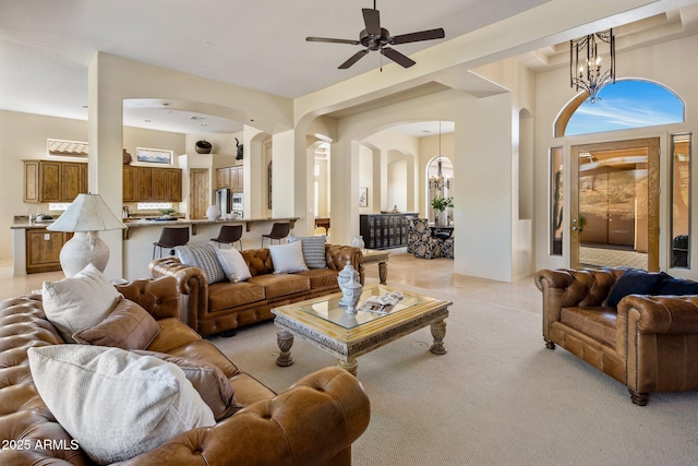 living area with arched walkways, ceiling fan with notable chandelier, and light carpet