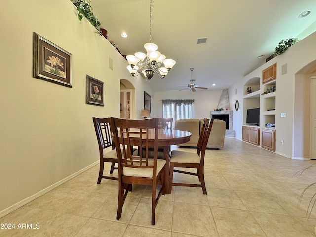 dining space with built in shelves, a fireplace, light tile patterned floors, and ceiling fan with notable chandelier