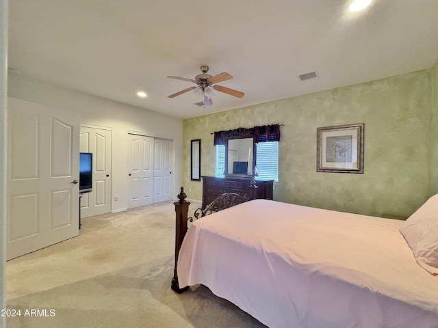 bedroom with ceiling fan, light carpet, and multiple closets