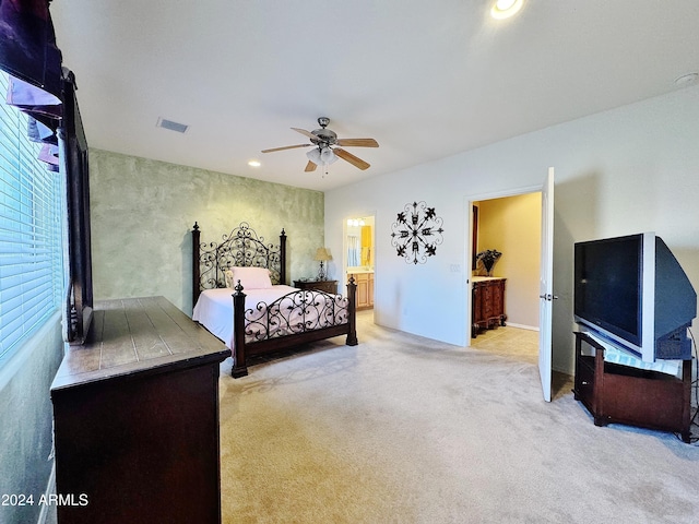 bedroom featuring light colored carpet, ensuite bath, and ceiling fan