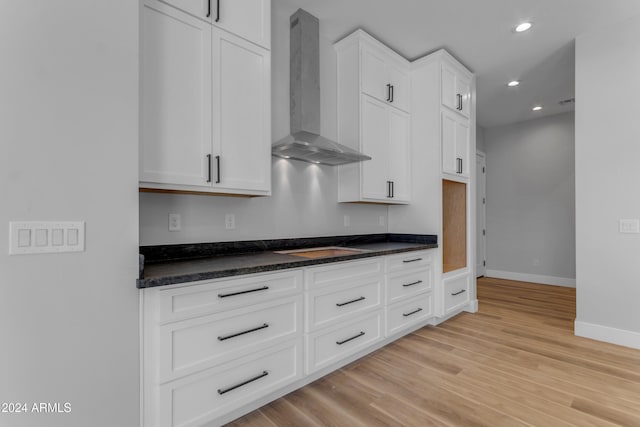 kitchen with light hardwood / wood-style floors, wall chimney range hood, and white cabinetry