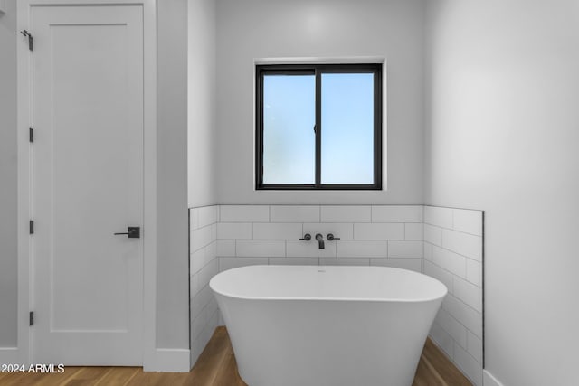 bathroom with hardwood / wood-style floors, a tub, and tile walls