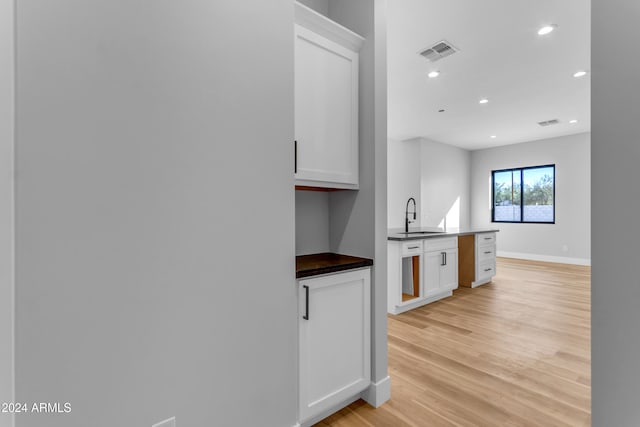 kitchen with white cabinetry, light wood-type flooring, and sink