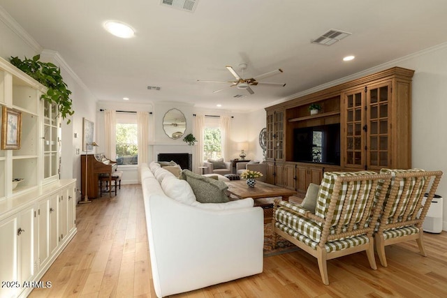 living room with ceiling fan, a fireplace, ornamental molding, and light hardwood / wood-style floors