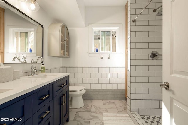 bathroom with tiled shower, a wealth of natural light, vanity, and toilet