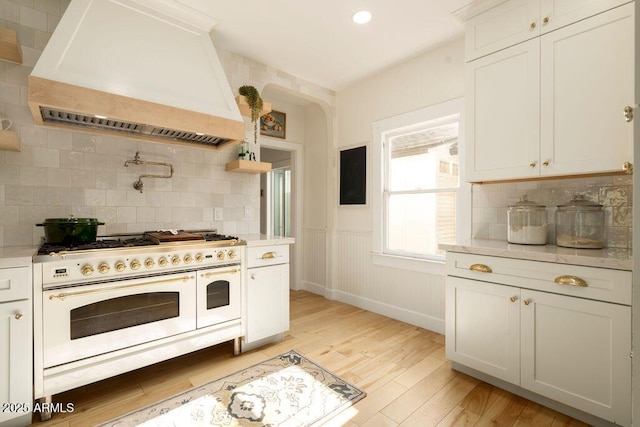 kitchen with range with two ovens, custom exhaust hood, white cabinets, and backsplash