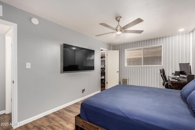 bedroom with baseboards, ceiling fan, radiator heating unit, wood finished floors, and a walk in closet