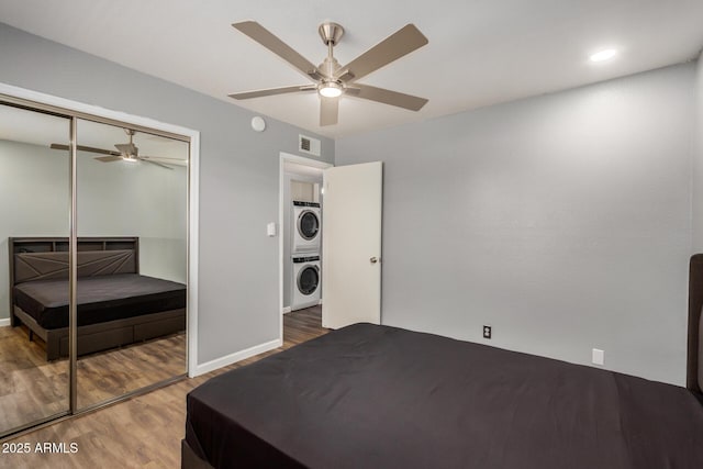 bedroom with stacked washer and dryer, visible vents, ceiling fan, wood finished floors, and a closet