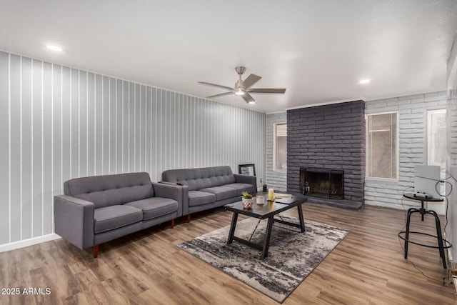 living room with ceiling fan, a fireplace, brick wall, and wood finished floors