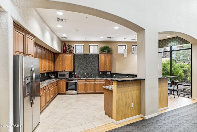 kitchen featuring brown cabinetry, visible vents, arched walkways, and appliances with stainless steel finishes