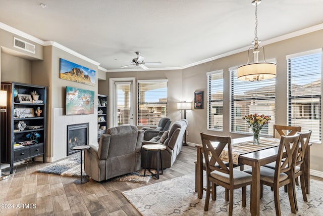 dining area featuring visible vents, a glass covered fireplace, a ceiling fan, wood finished floors, and crown molding