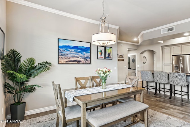 dining room with crown molding, light wood-type flooring, arched walkways, baseboards, and visible vents