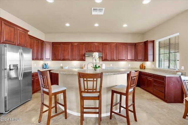 kitchen with light stone countertops, a kitchen bar, light tile floors, and stainless steel fridge