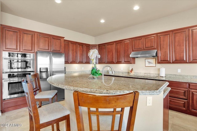 kitchen with a kitchen breakfast bar, stainless steel appliances, light tile floors, a center island with sink, and light stone counters